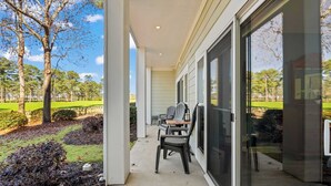 Une terrasse couverte avec deux fauteuils Adirondack et une table, donnant sur un terrain de golf.