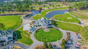 Vue aérienne d’un terrain de golf avec un club-house, des aires de stationnement et un étang.