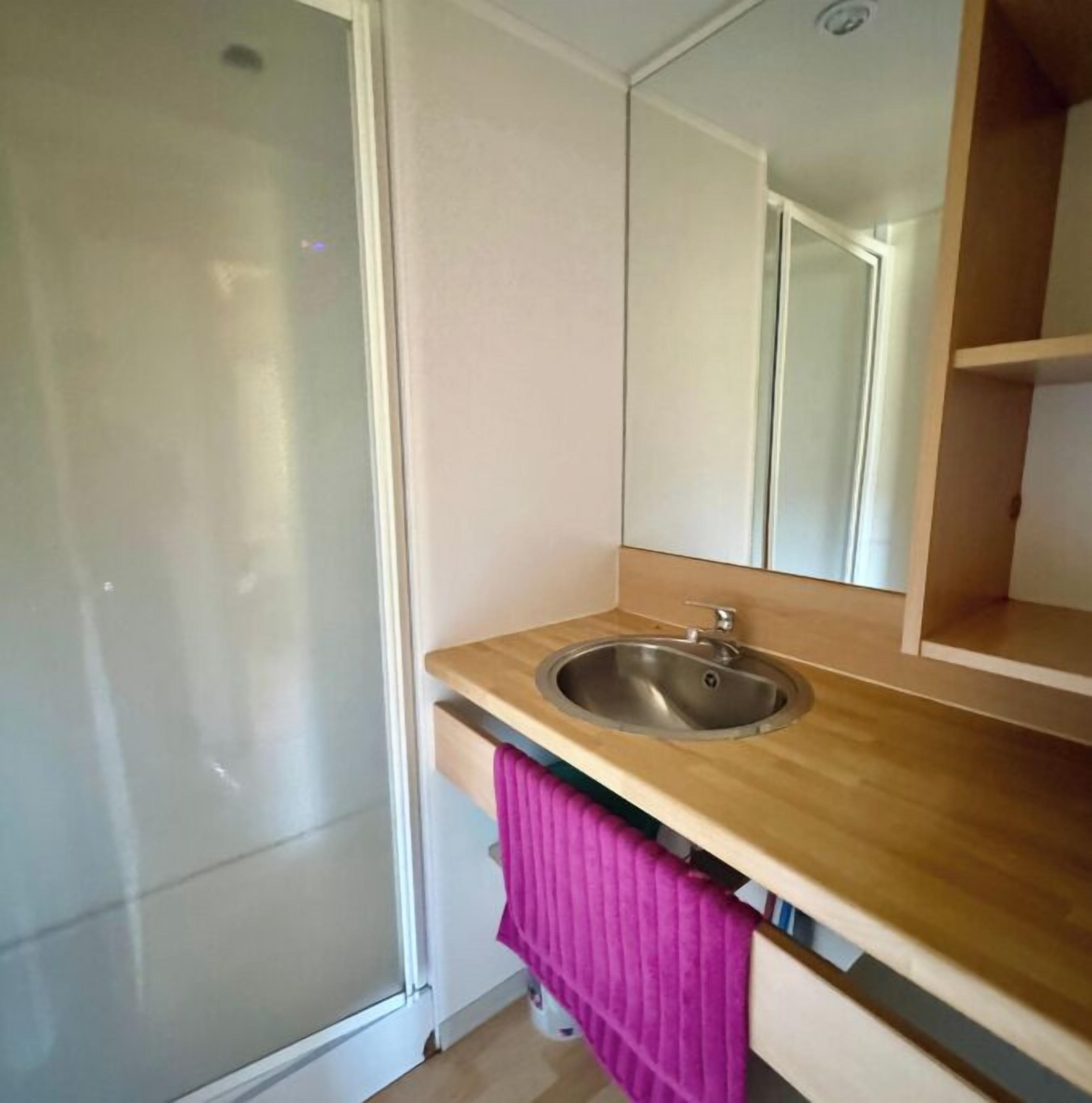 A bathroom with a wooden vanity, a sink, a mirror, and a pink towel.