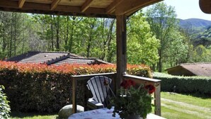 A covered outdoor seating area with a table and chairs, surrounded by lush greenery and a view of a mountain range. - Chalet 1 en Cévennes (Aulas)