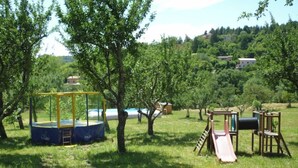 A playground with a trampoline and slides in a grassy area with trees and houses in the background. - Chalet 1 en Cévennes (Aulas)
