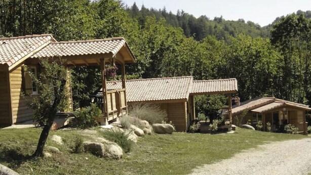 A rustic cabin with a tiled roof and a wooden porch, surrounded by a gravel path and greenery. - Chalet 1 en Cévennes (Aulas)