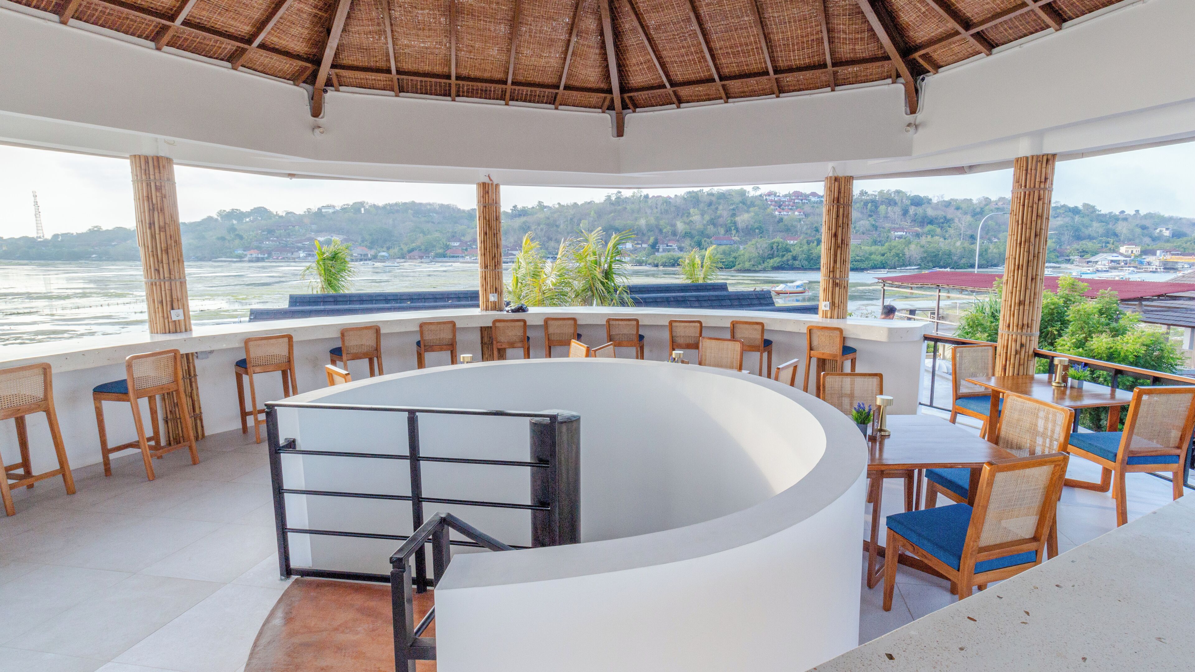 A restaurant with a curved white counter, wooden chairs, and a view of a river and hills.