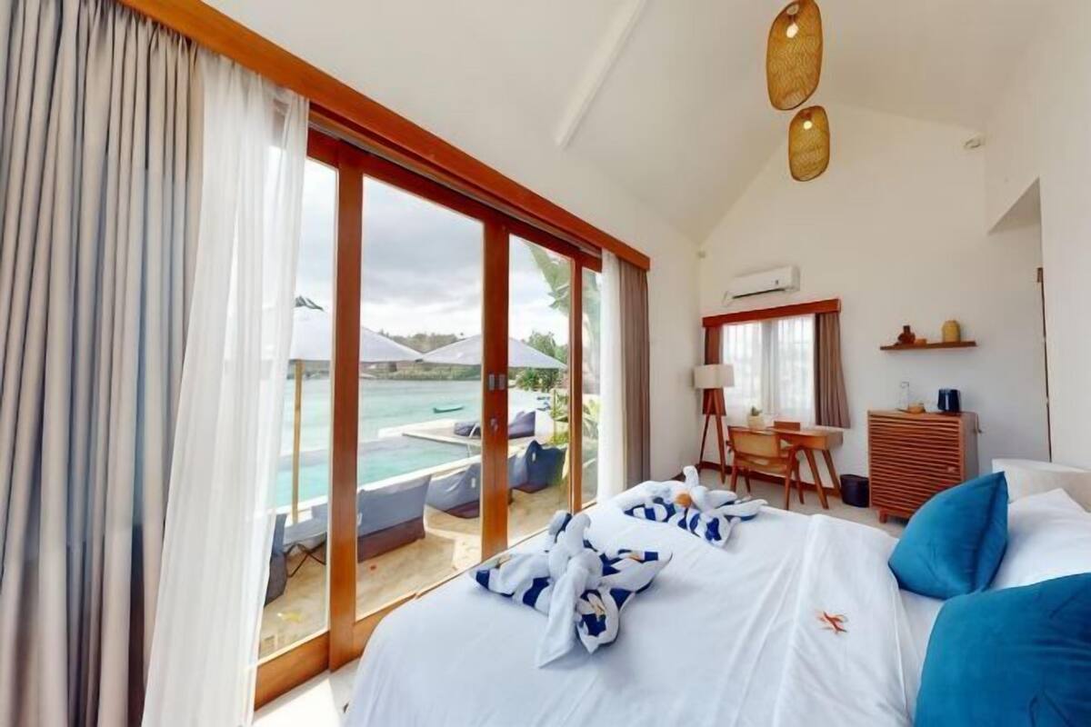A bedroom with a bed, a desk, and a view of the ocean.