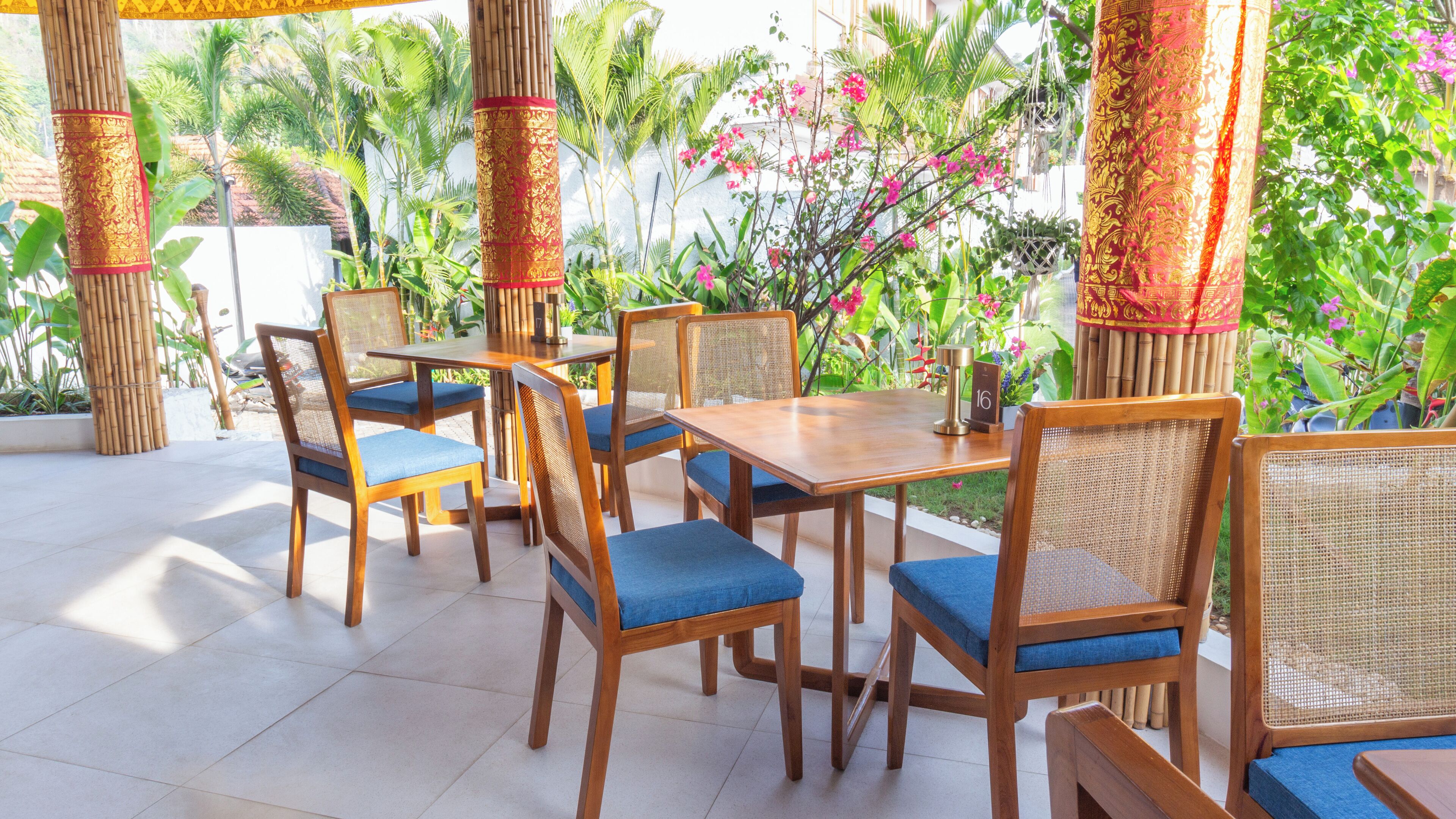 A wooden table with blue cushioned chairs, surrounded by bamboo pillars and lush greenery.