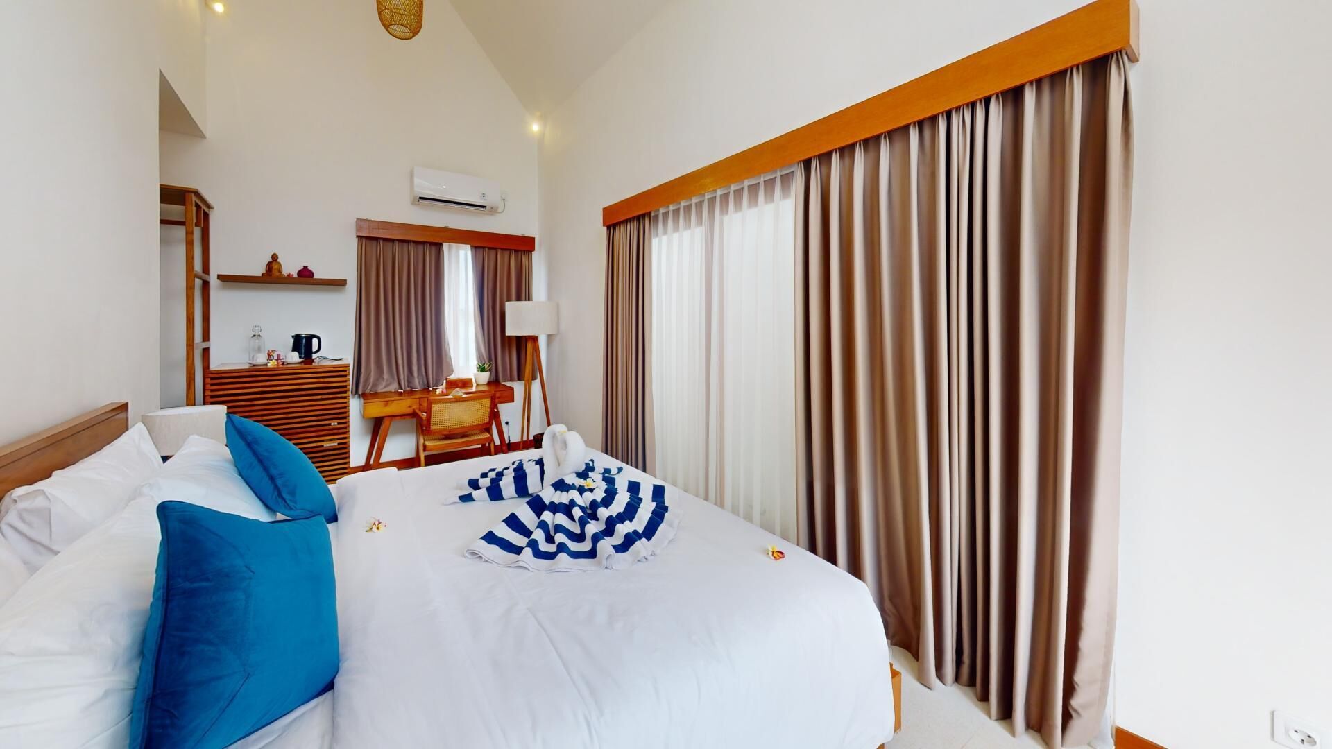 A hotel room with a bed, a desk, a chair, a lamp, and curtains.