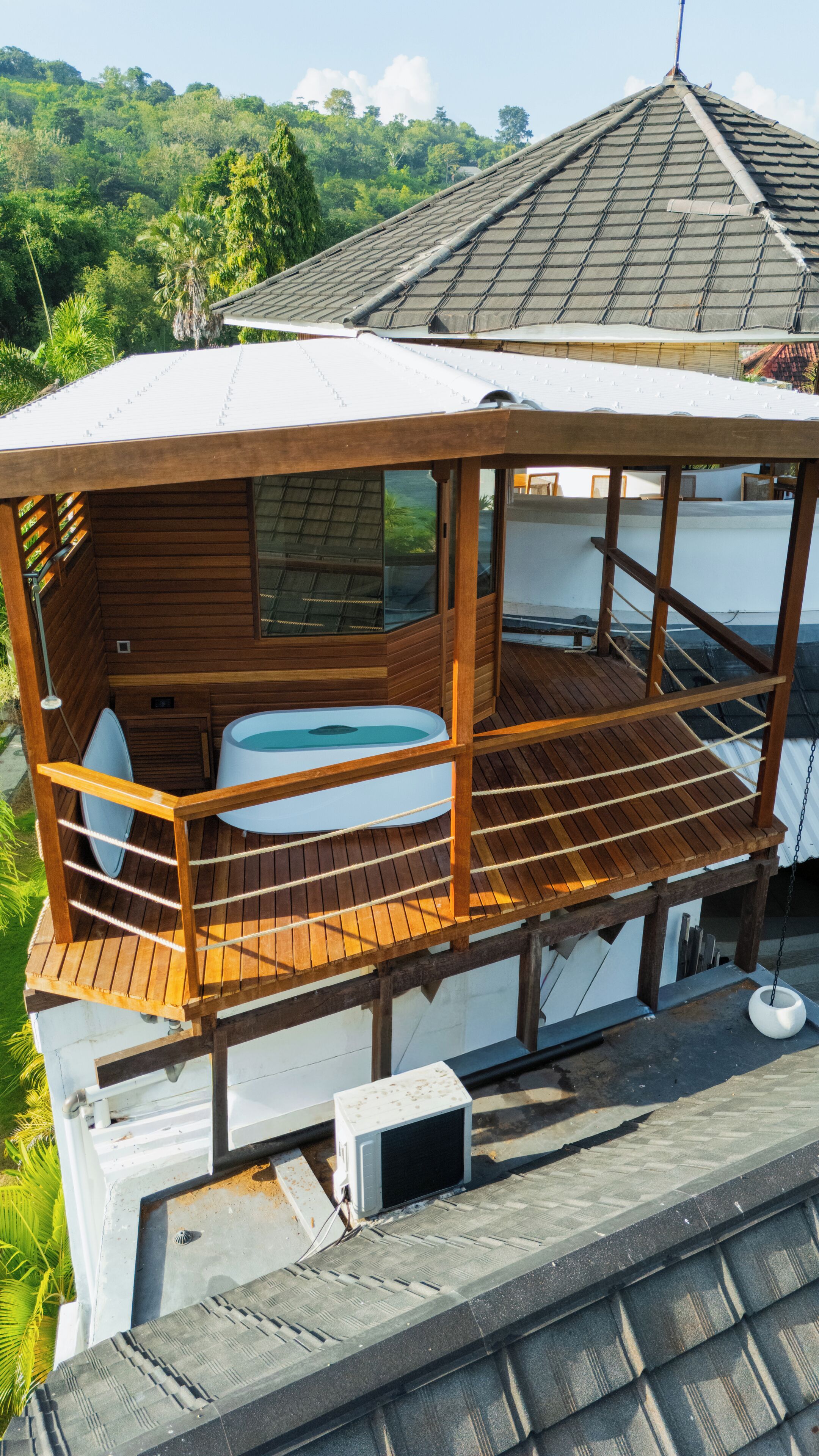 A wooden deck with a hot tub, a small enclosed area, and a view of the surrounding greenery.