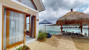 Un hotel frente a la playa con una sombrilla de paja, una zona de piscina y vistas al mar.