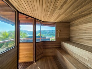 A sauna room with wooden walls and a large window offering a view of a tropical landscape. - Segara Seaside Resort (Ceningan Island)