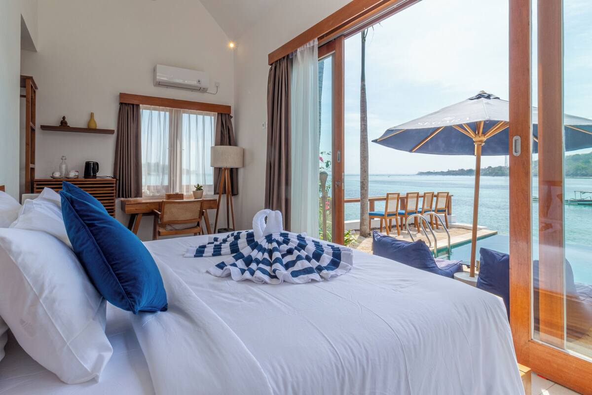 A hotel room with a bed, a desk, a chair, and a view of the sea.