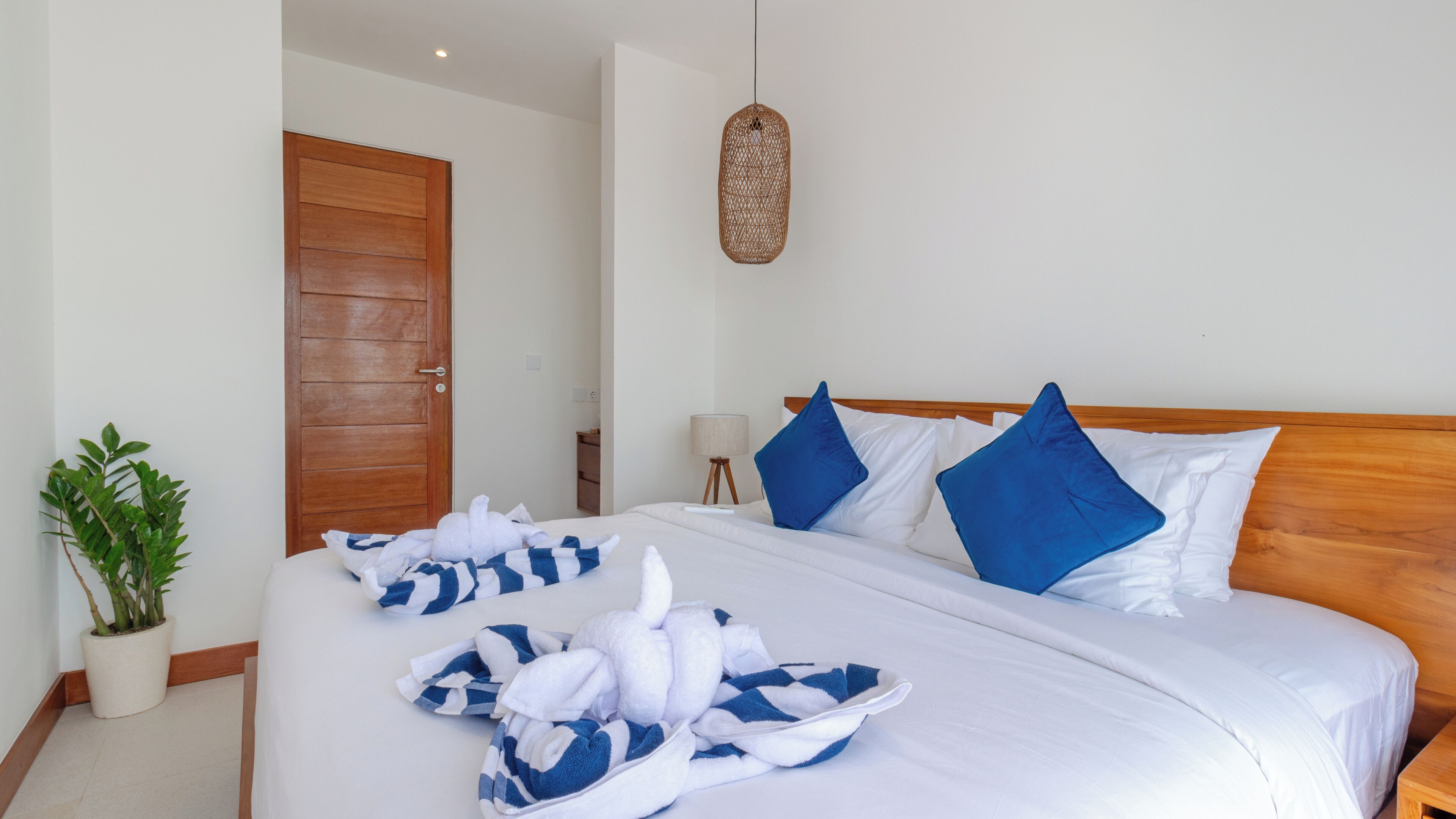 Une chambre d’hôtel avec un grand lit, une porte en bois, un luminaire suspendu et une plante en pot.