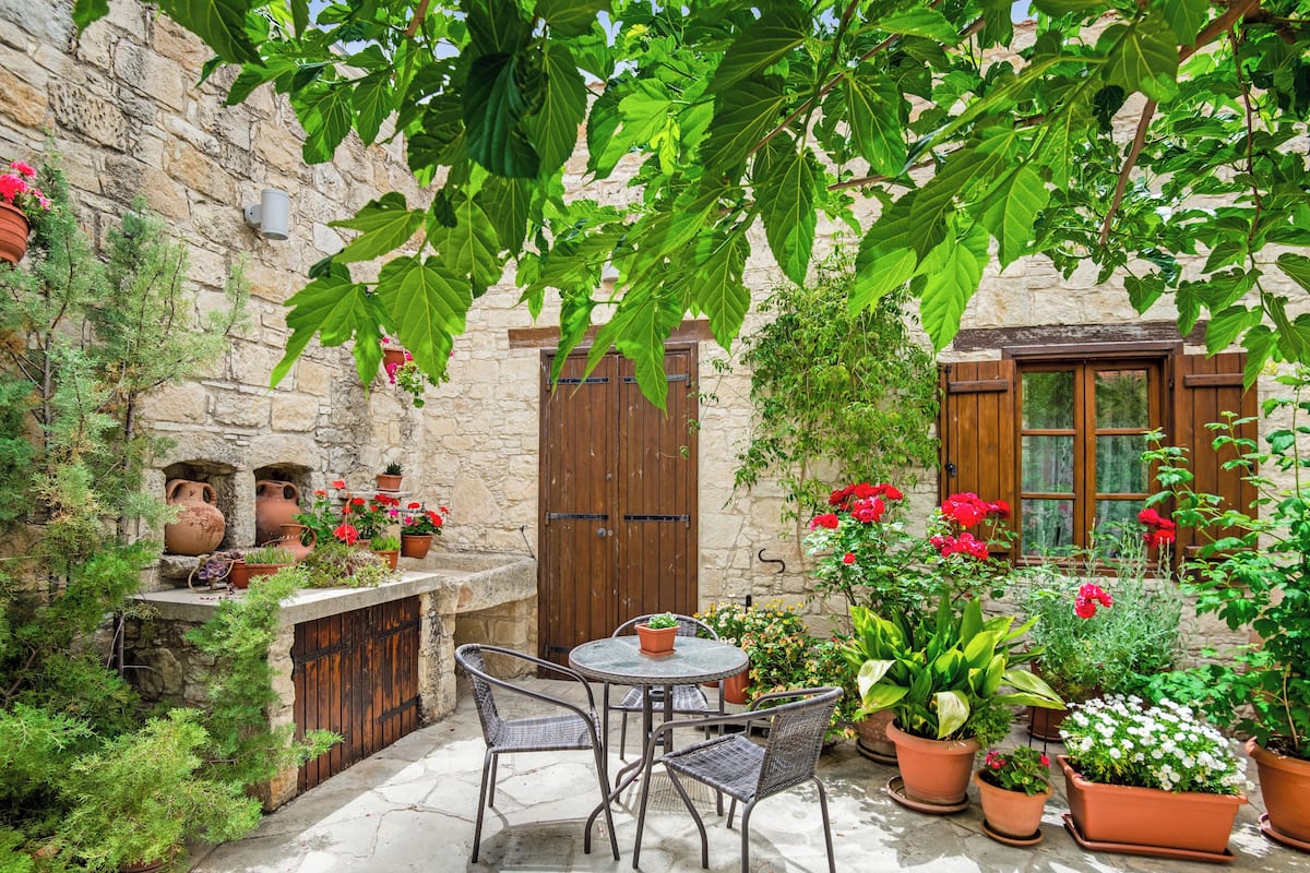 Un patio de piedra con una mesa y sillas, rodeado de plantas y flores en macetas.