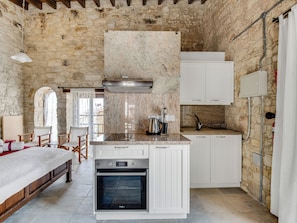 A compact kitchen with a built-in oven, white cabinetry, and a stone wall backdrop. - Arsorama Village Homes (Arsos)