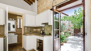 A compact kitchen with white cabinets, a built-in oven, and a large window opening to a garden. - Arsorama Village Homes (Arsos)
