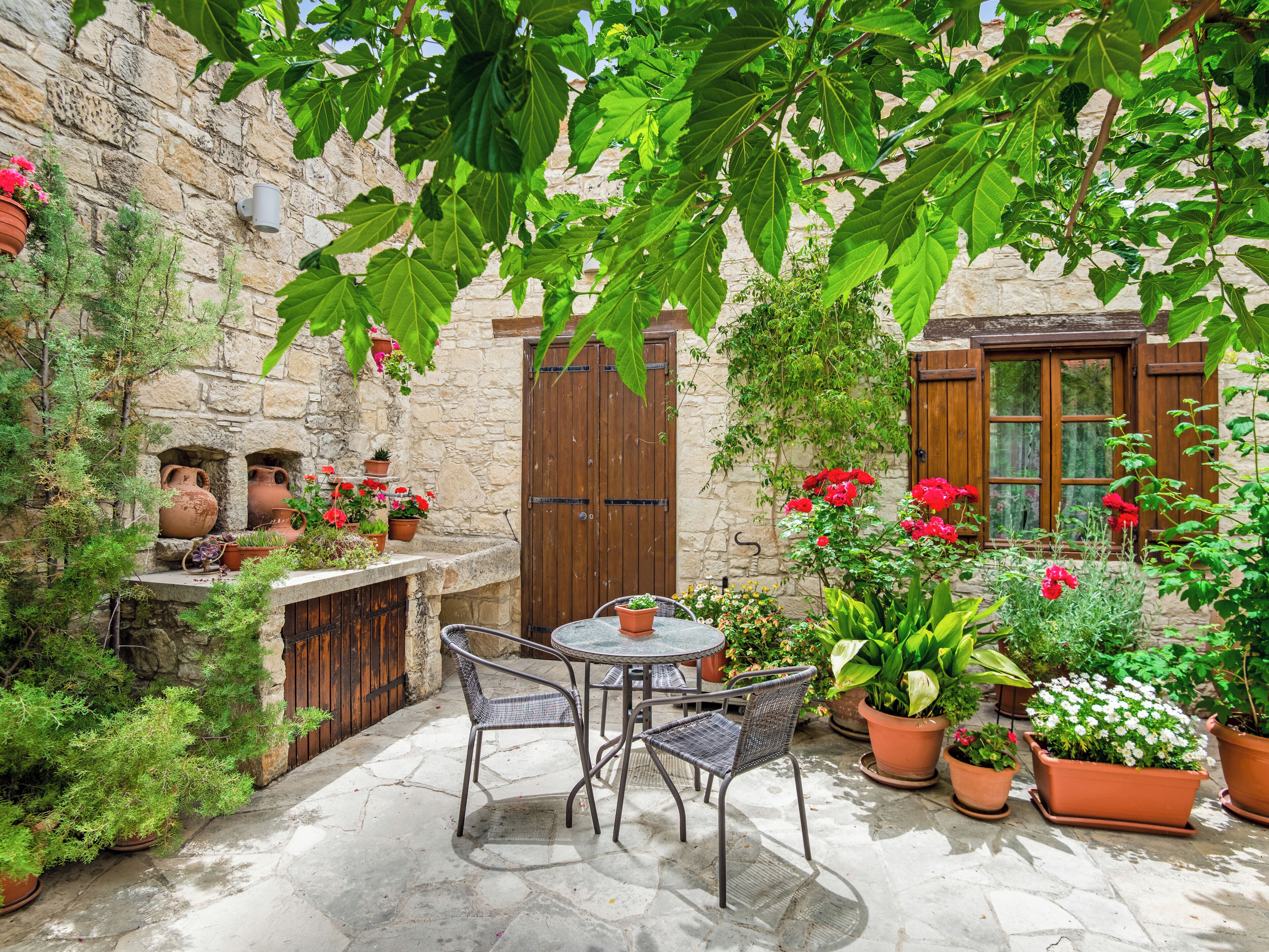 Un patio de piedra con una mesa y sillas, rodeado de plantas y flores en macetas.