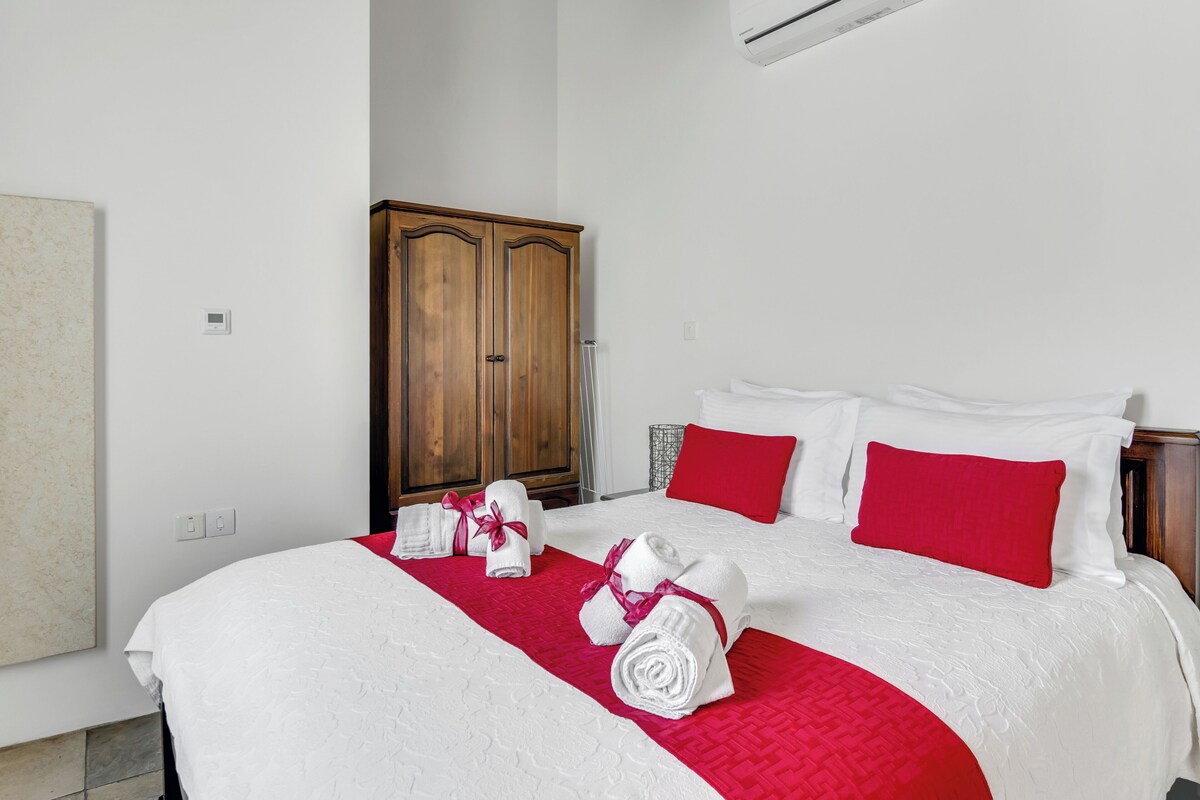 A hotel room with a large bed, red and white bedding, a wooden wardrobe, and a wall-mounted air conditioner.