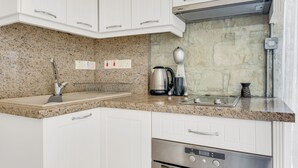 A modern kitchen with white cabinets, granite countertops, a stainless steel range hood, and a built-in oven. - Arsorama Village Homes (Arsos)