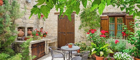 A stone courtyard with a table and chairs, surrounded by potted plants and flowers.