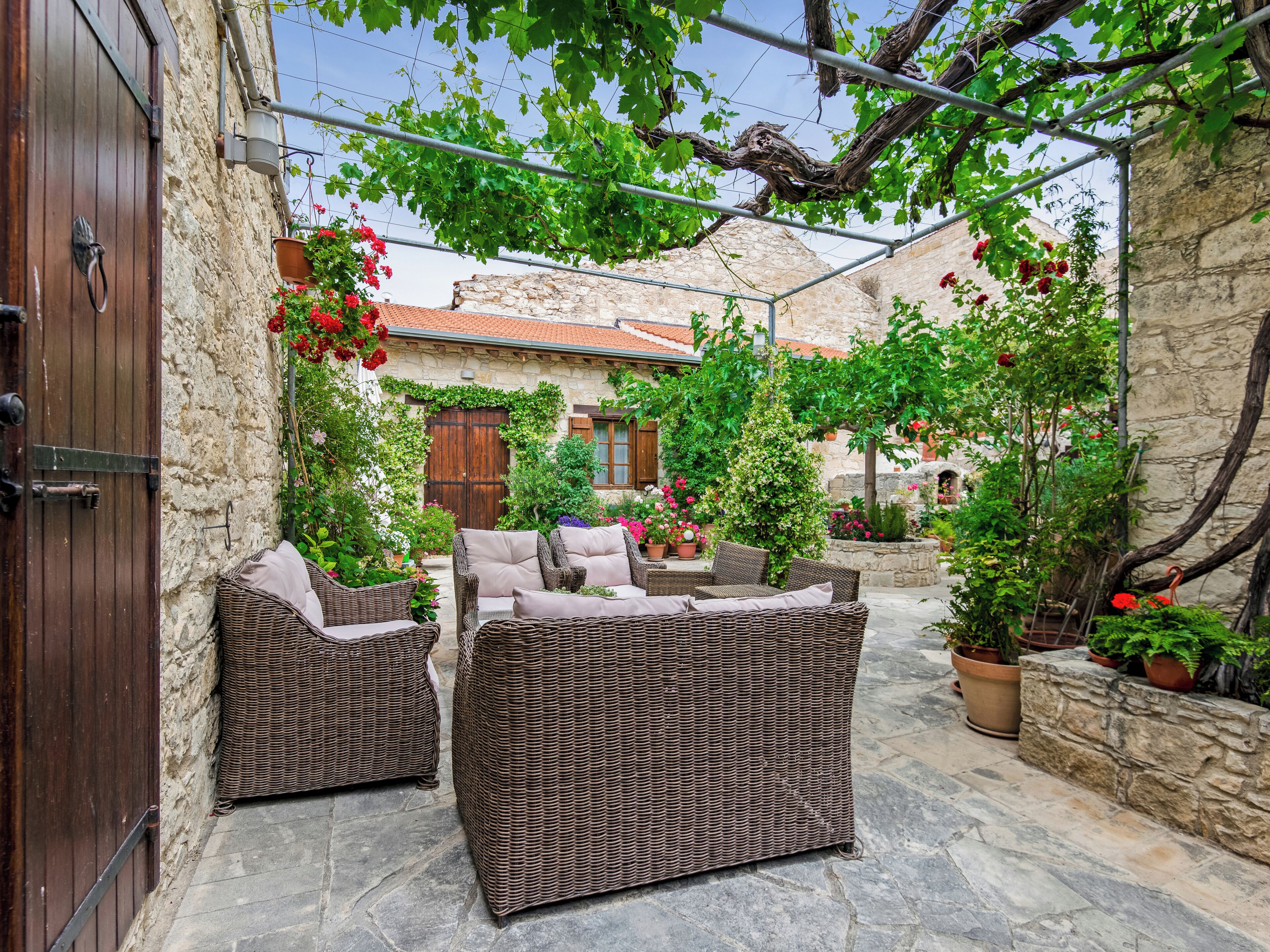 A courtyard with wicker furniture, stone walls, and potted plants.