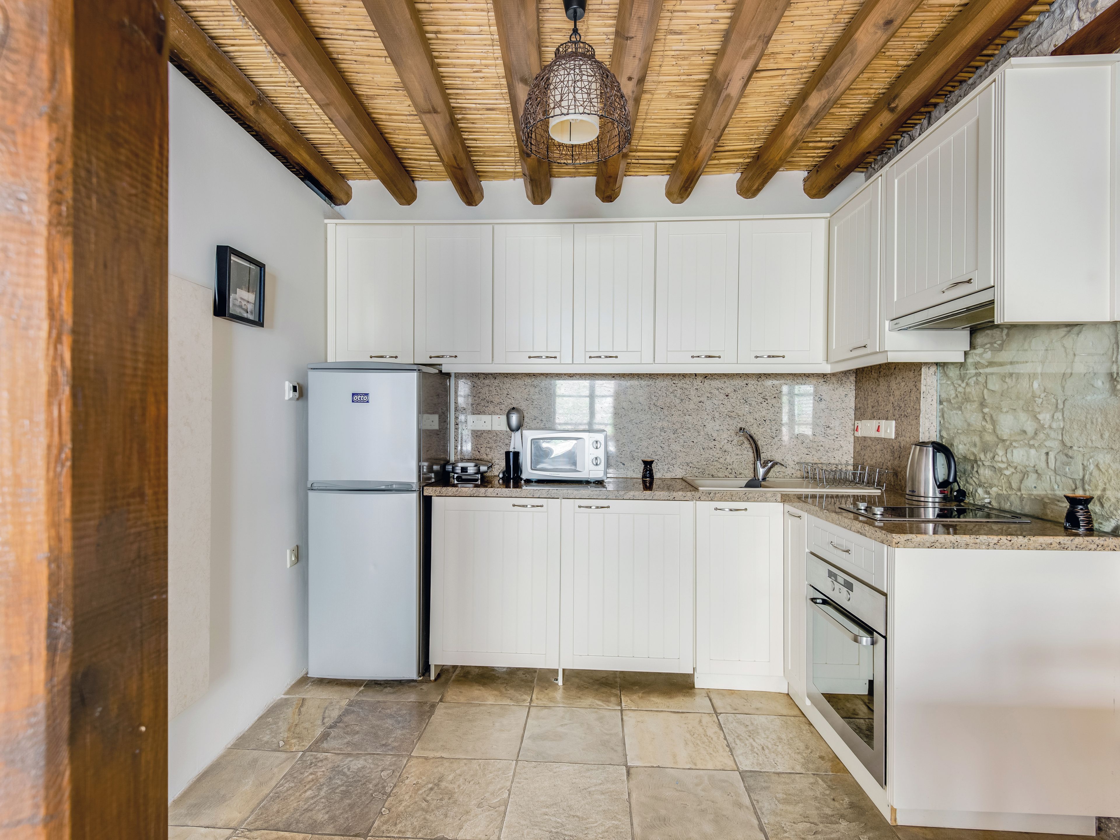 Una cocina con armarios blancos, horno empotrado, microondas y refrigerador.
