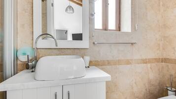 Un baño con lavamanos blanco, espejo y mueble. Hay un perchero sobre el lavamanos y un inodoro a la derecha.