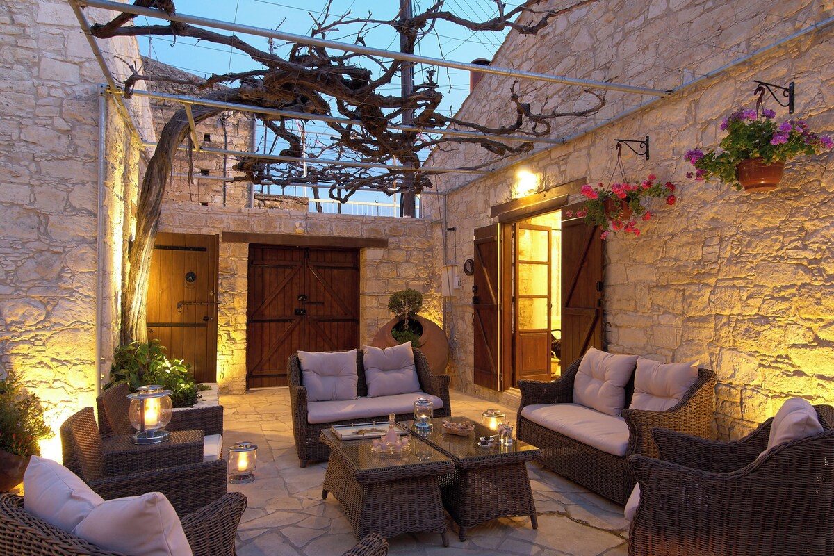 An outdoor patio with wicker furniture, stone walls, and a wooden door.
