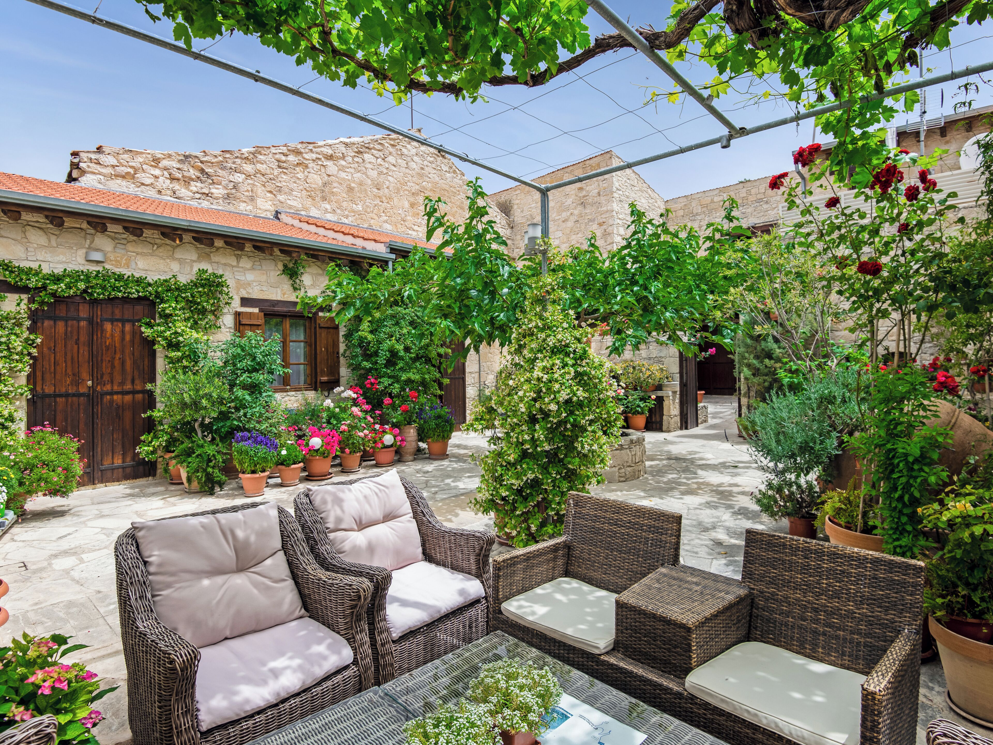 Un patio con mobiliario de mimbre, plantas en macetas y un edificio de piedra.