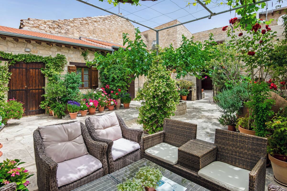 Un patio con mobiliario de mimbre, plantas en macetas y un edificio de piedra.