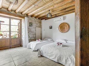 A room with two beds, stone walls, a wooden ceiling, and a large window. - Arsorama Village Homes (Arsos)