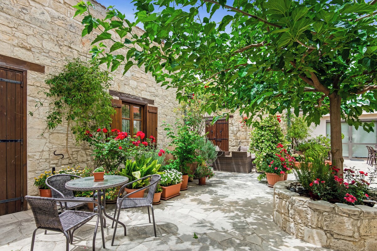 A courtyard with stone walls, a wooden door, potted plants, and outdoor furniture.