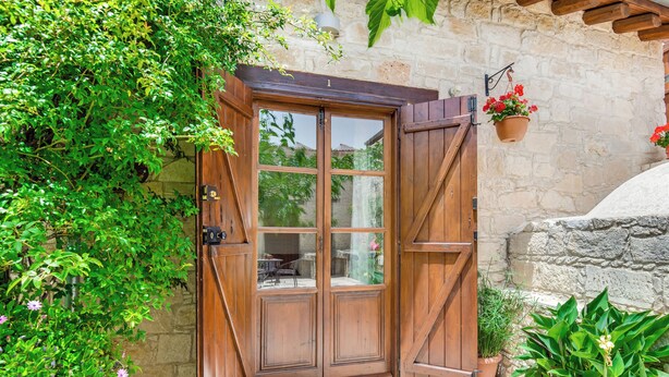 A wooden door with glass panels, a stone wall, and potted plants. - Arsorama Village Homes (Arsos)