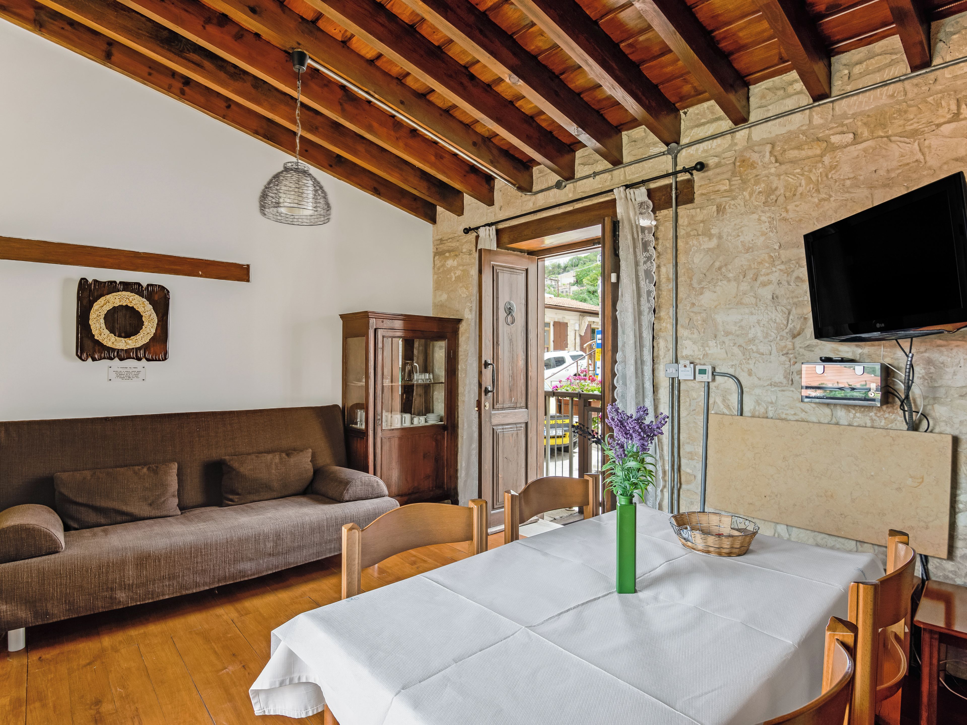 A cozy living room with a wooden ceiling, a stone wall, a wooden cabinet, a sofa, a dining table with a white tablecloth, and a green vase.