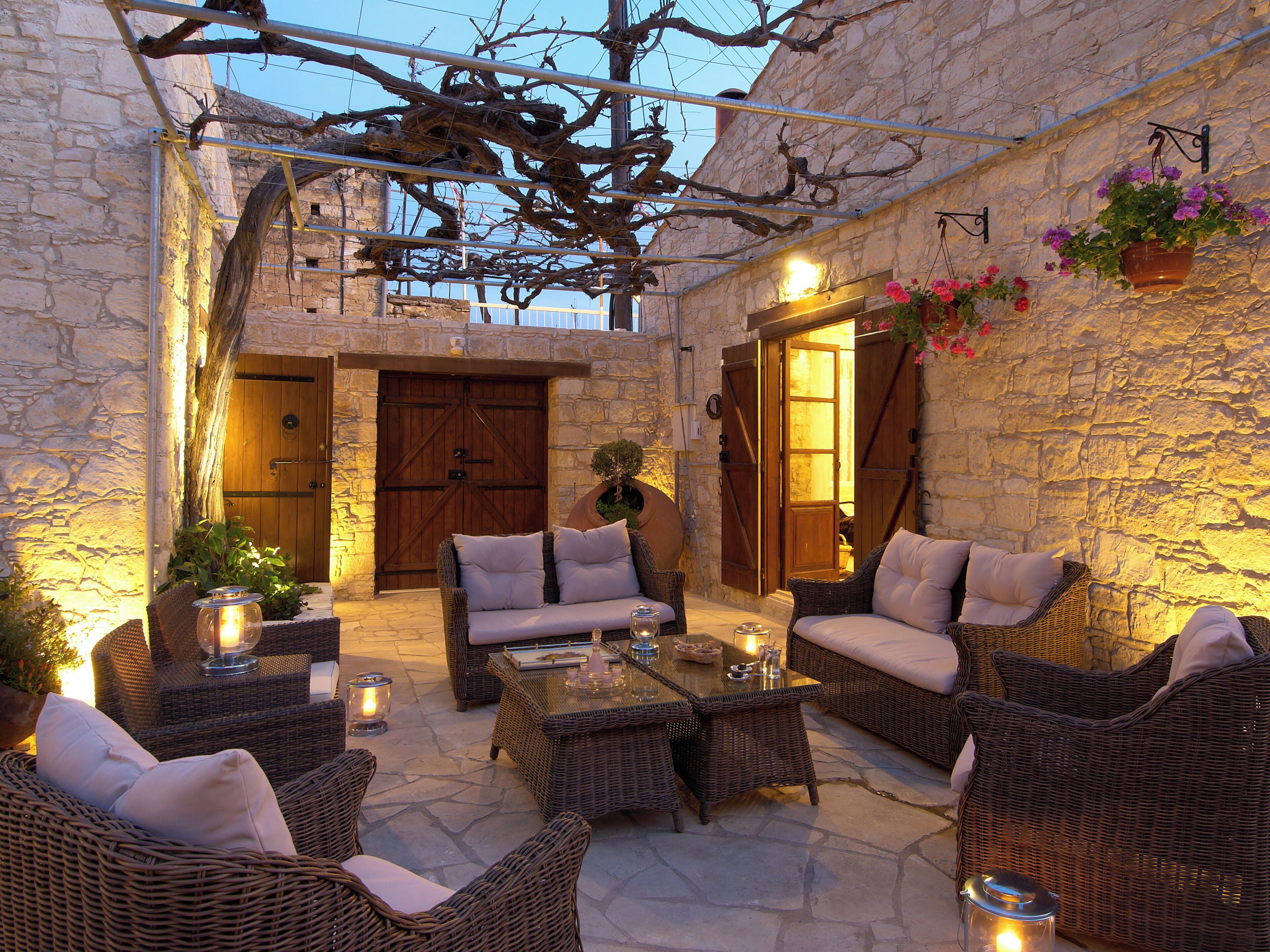 Un patio al aire libre con mobiliario de mimbre, paredes de piedra y una puerta de madera.