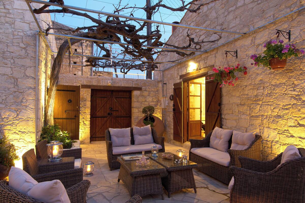 Un patio al aire libre con mobiliario de mimbre, paredes de piedra y una puerta de madera.