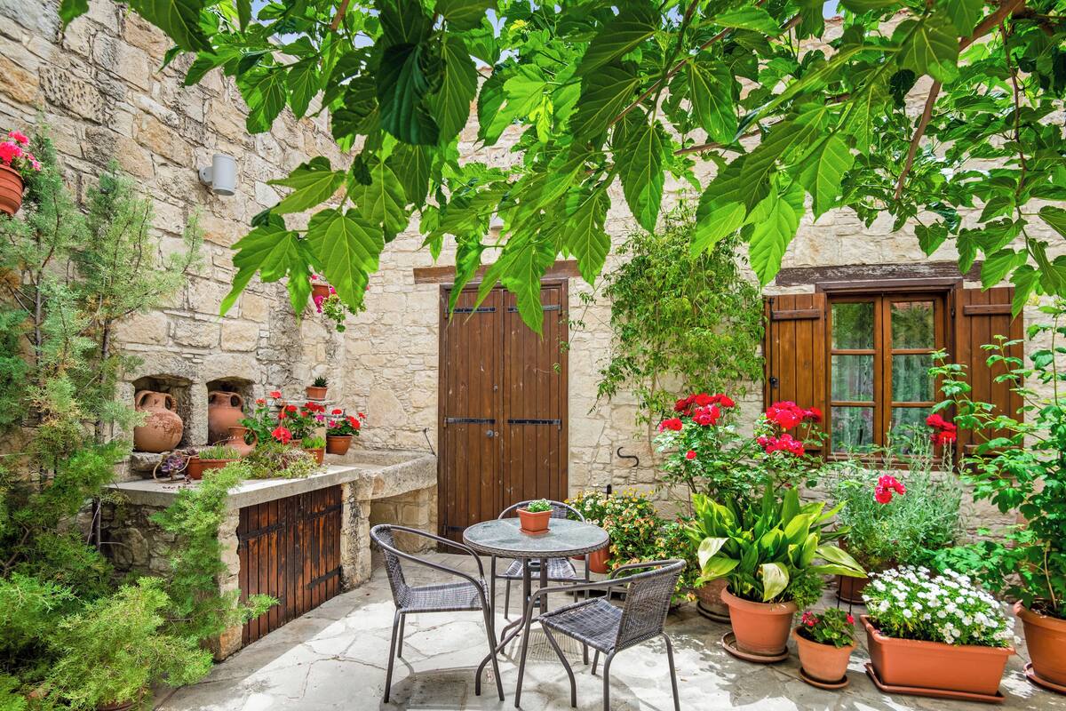 A stone courtyard with a table and chairs, surrounded by potted plants and flowers.