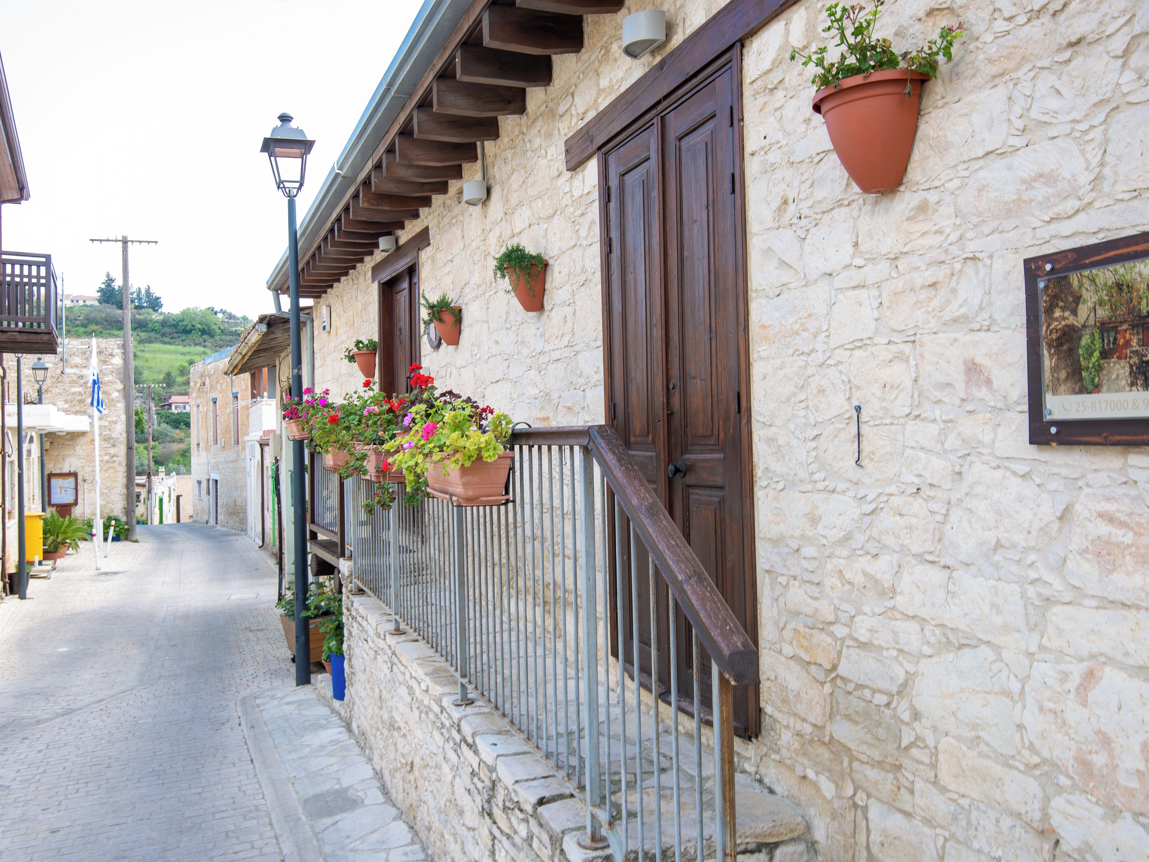 A stone building with wooden doors and windows, potted plants on the balcony, and a cobblestone street.