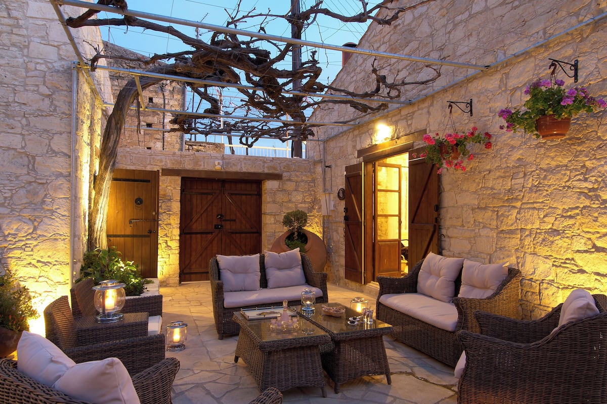 Un patio al aire libre con mobiliario de mimbre, paredes de piedra y una puerta de madera.