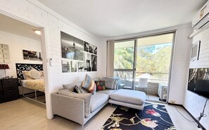 Een moderne woonkamer met een grijze bank, een bijzettafeltje en een groot raam met uitzicht op bomen.