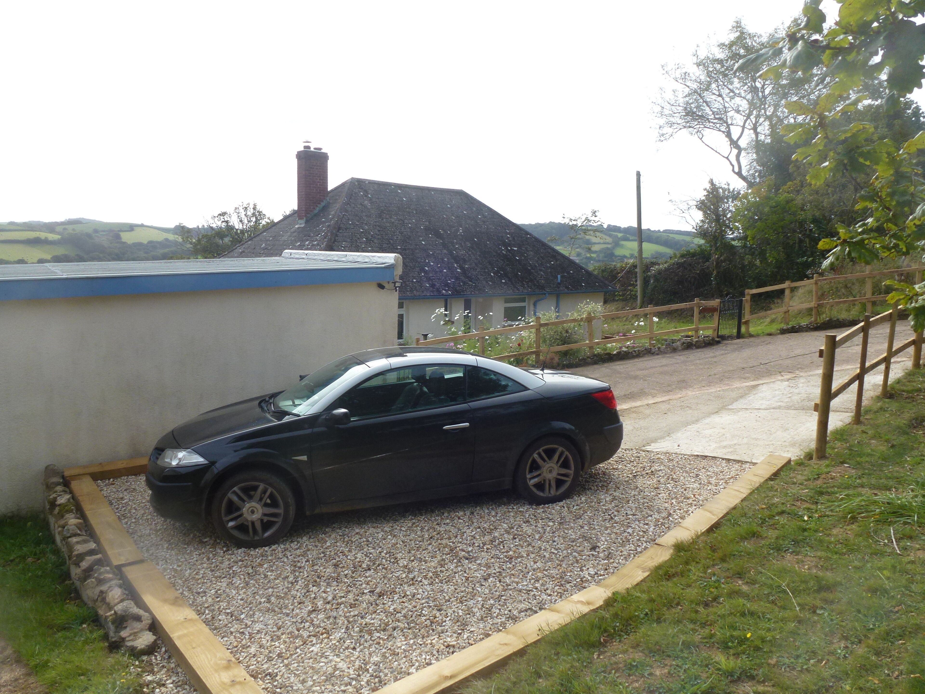 A black car parked in a gravel driveway with a house in the background.