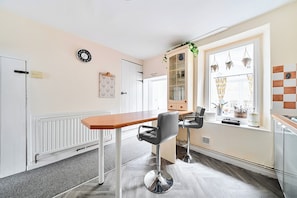 Een moderne keuken met een houten tafel, twee barkrukken, een klok, een kast met glazen deuren en een raam met gordijnen.
