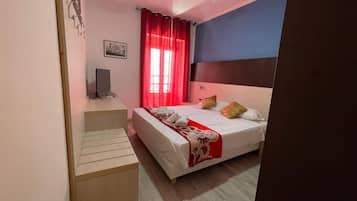Quarto com cama, escrivaninha, cadeira, ventilador de teto e janela com cortinas vermelhas.