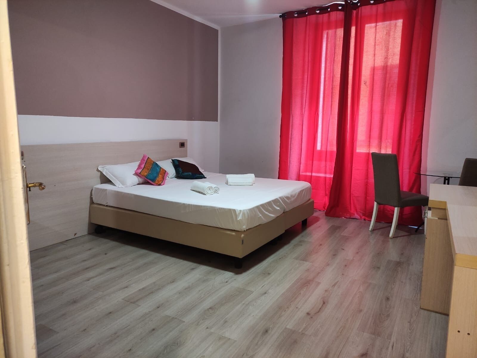 A bedroom with a bed, a chair, a desk, and a red curtain.