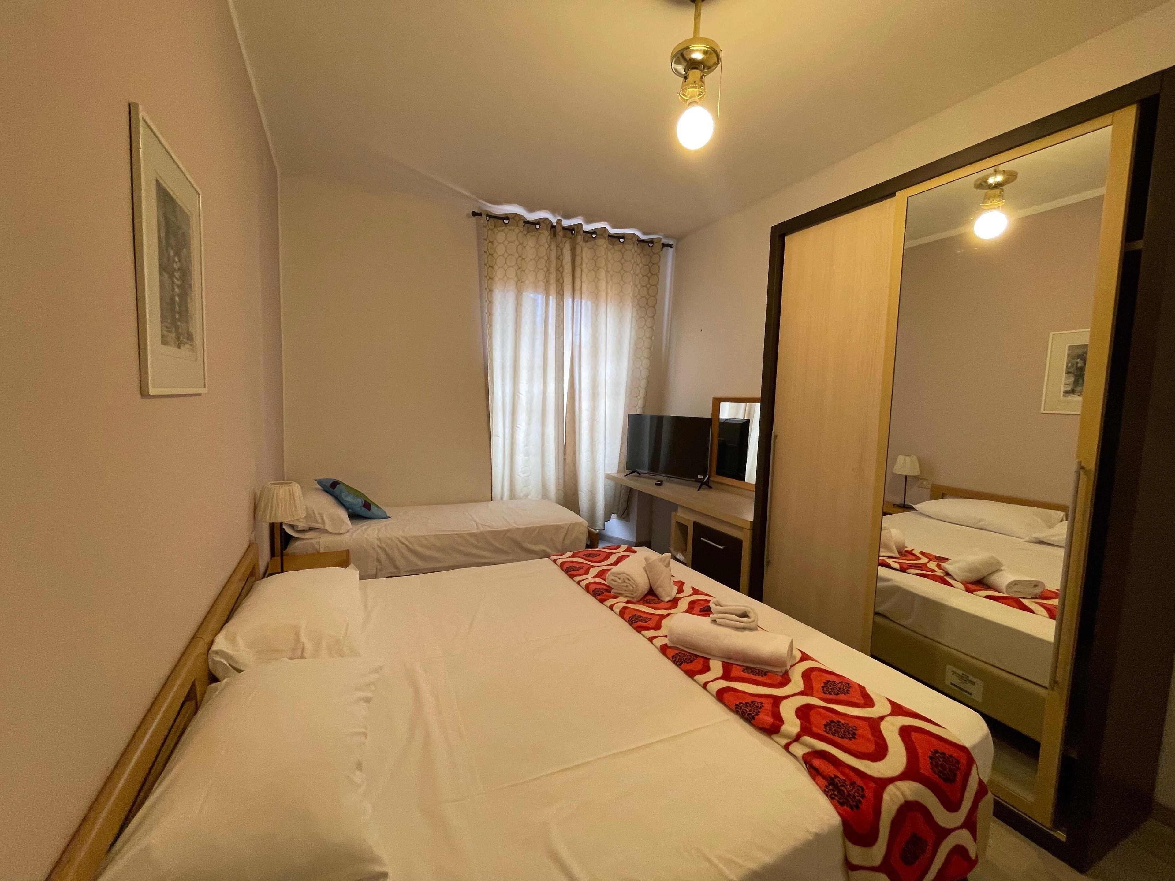 A hotel room with two single beds, a TV, a mirror, and a wardrobe.