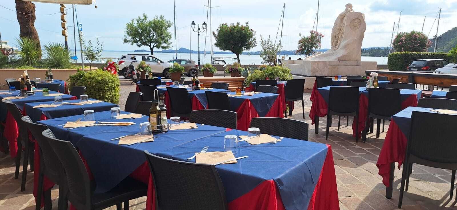 An outdoor dining area with tables set for two, covered with blue tablecloths and red napkins.