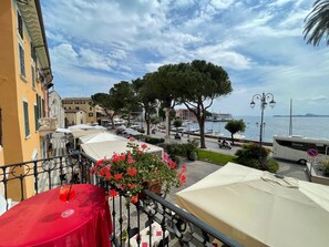 A balcony with a red tablecloth, a flower arrangement, and a view of a marina with boats and a building in the background. - Hotel & Restaurant San Marco AB (Toscolano Maderno)