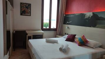 Una habitación de hotel con una cama, un escritorio, una silla, una ventana y un cuadro en la pared.