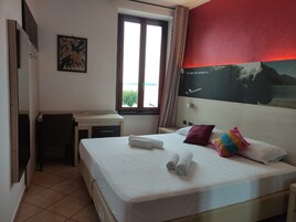 Una habitación de hotel con una cama, un escritorio, una silla, una ventana y un cuadro en la pared.