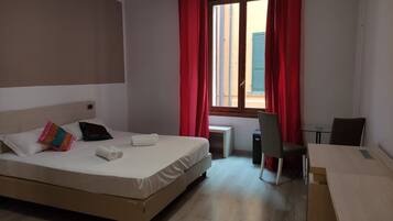 A hotel room with a bed, a desk, a chair, and a window with red curtains.