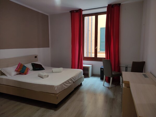 A hotel room with a bed, a desk, a chair, and a window with red curtains. - Hotel & Restaurant San Marco AB (Toscolano Maderno)