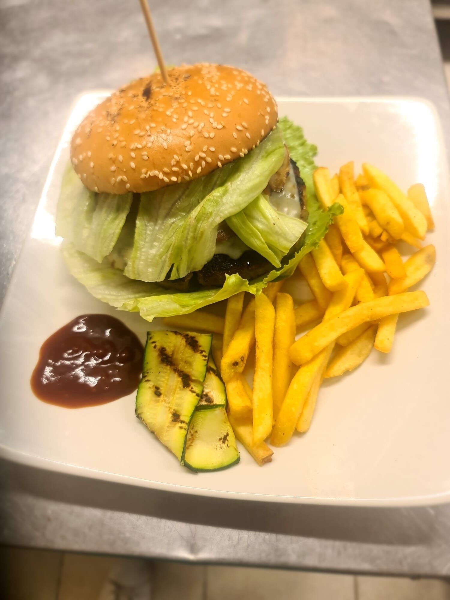 A plate with a hamburger, French fries, and grilled zucchini slices.